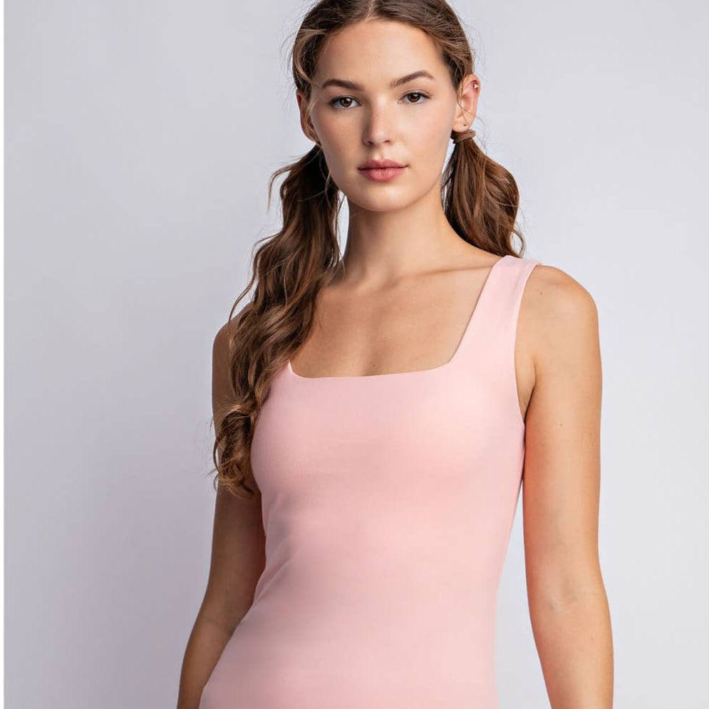 A woman wearing a square neckline, sleeveless pink tank top paired with pants.